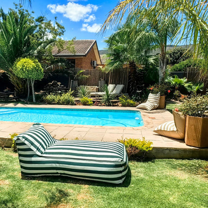 Green Striped daybed lounger by a pool with palm trees and a house in the background