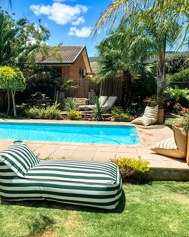 Green Striped daybed lounger by a pool with palm trees and a house in the background