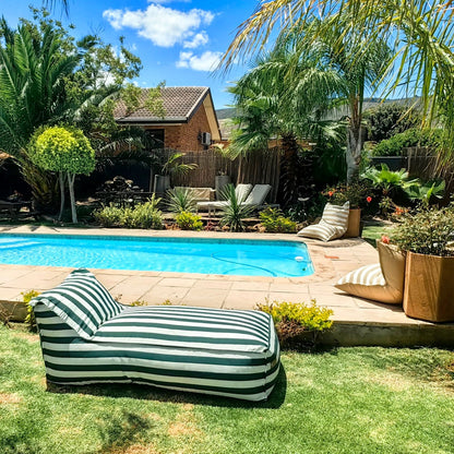 Green Striped daybed lounger by a pool with palm trees and a house in the background