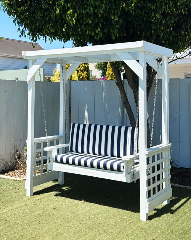 White wooden swing with black and white striped cushion in a backyard setting.
