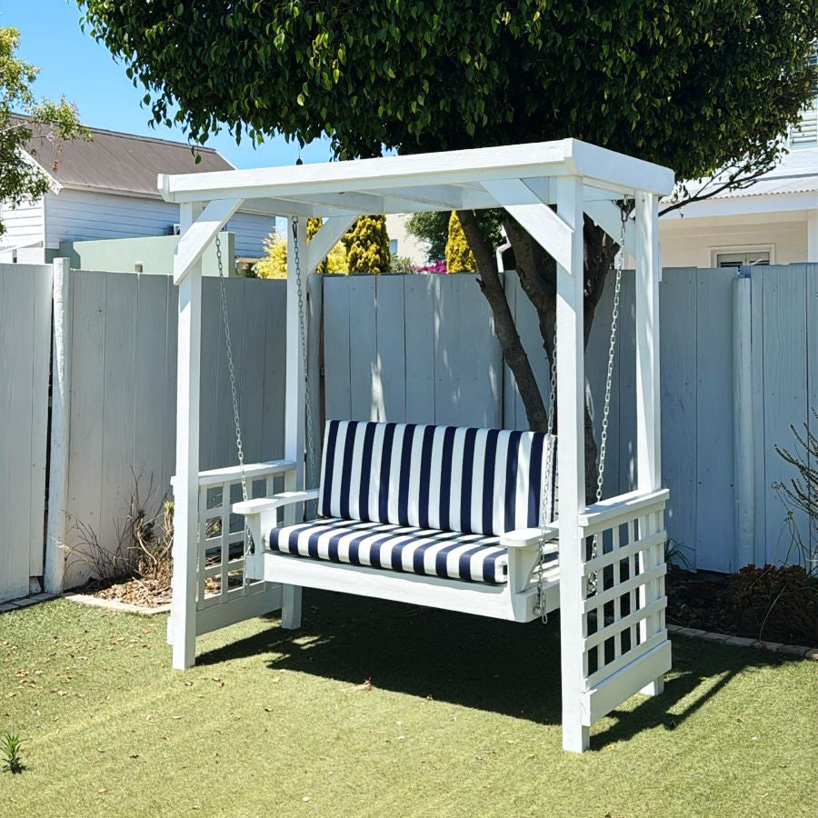 White wooden swing with black and white striped cushion in a backyard setting.