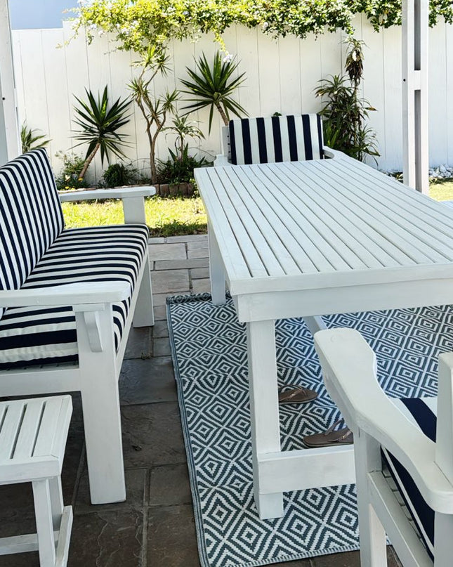 Outdoor patio with white table and chairs with black and white striped cushions, under a white pergola.