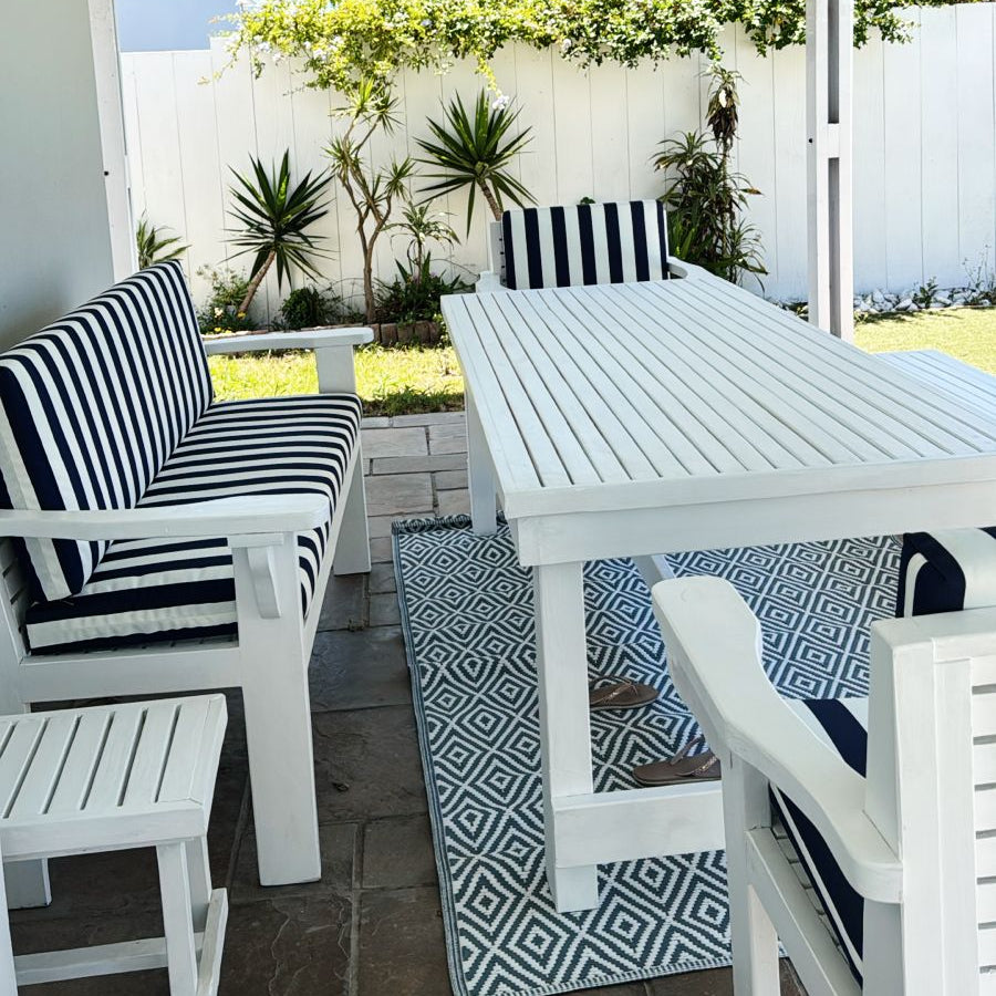 Outdoor patio with white table and chairs with black and white striped cushions, under a white pergola.