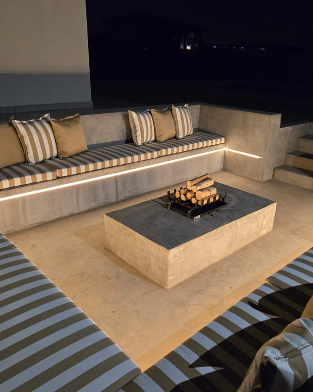 Modern outdoor seating area with striped cushions, a fire pit table, and a large screen TV.