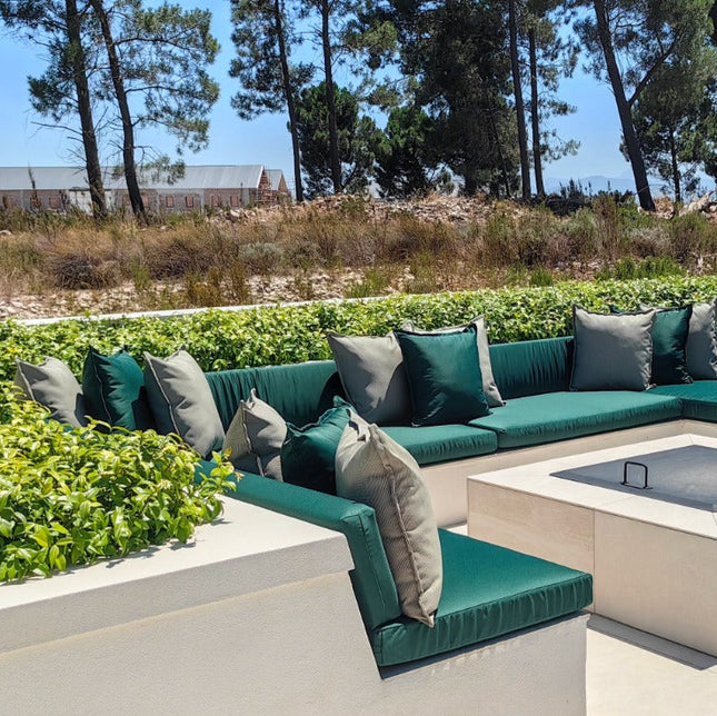 Outdoor patio with modern sectional sofa and fire pit table surrounded by greenery.
