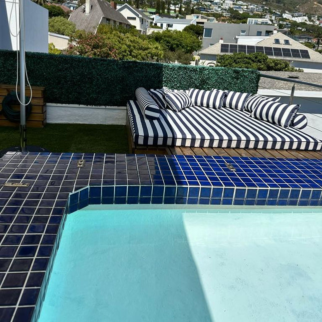 Outdoor seating area with striped cushions by a pool, featuring a mountainous landscape in the background.
