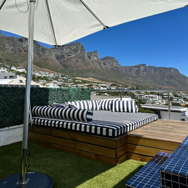 Outdoor seating area with striped cushions under a large umbrella, Table Mountain in the background.